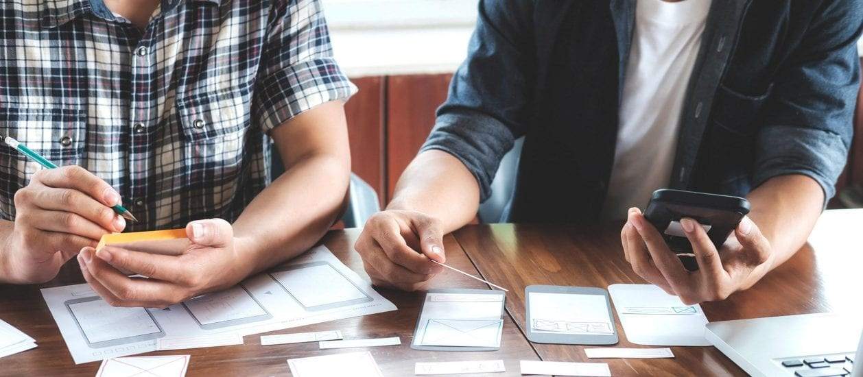 Two people collaboarting at a desk with paper prototypes