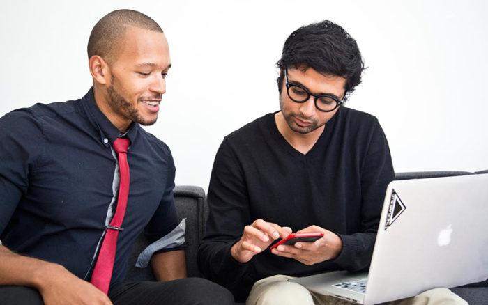  Two men sitting next to each other looking at a phone. 