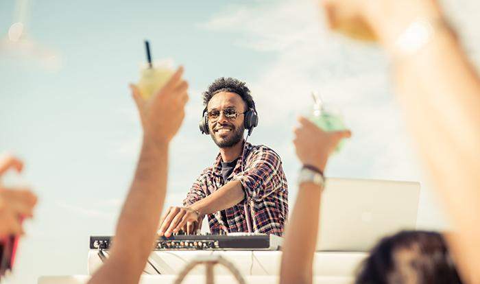 Man DJing with people raising their glasses in the air. 