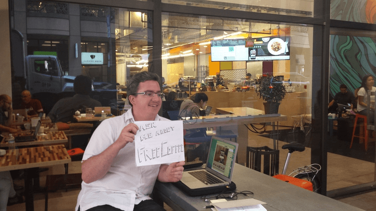 Man at cafe holding sign soliciting people to test his software