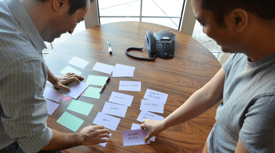 Two men using index cards doing a card sorting exercise on a table.