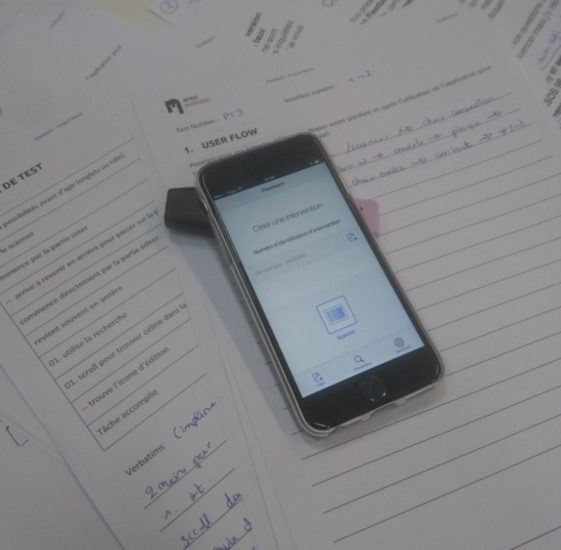 An old iPhone, with an app interface displayed, sits atop a stack of papers.