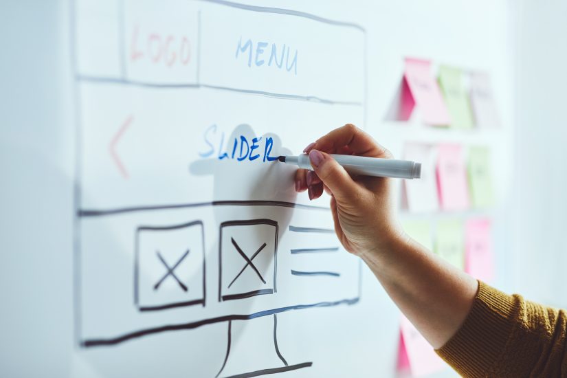 Female web developer with blue marker planning website on whiteboard. 