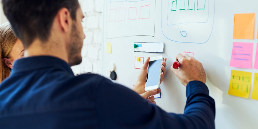 UX designers collaborate on a mobile interface using a whiteboard.