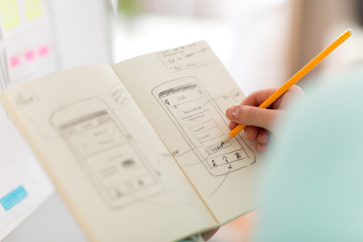 A designer sketching a low-fidelity wireframe in a sketchbook.
